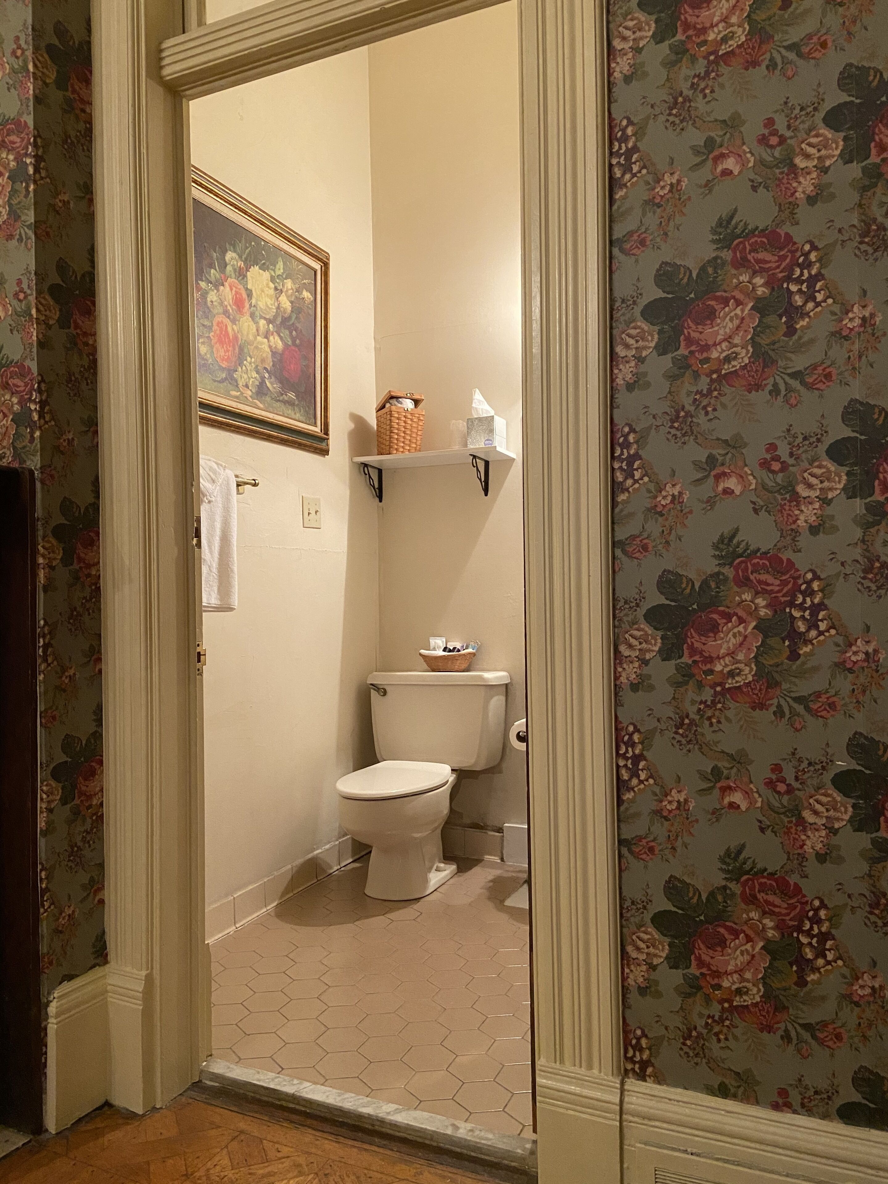 A bathroom with a toilet, a basket on the shelf, and a floral wallpaper.