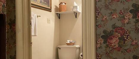A bathroom with a toilet, a basket on the shelf, and a floral wallpaper.