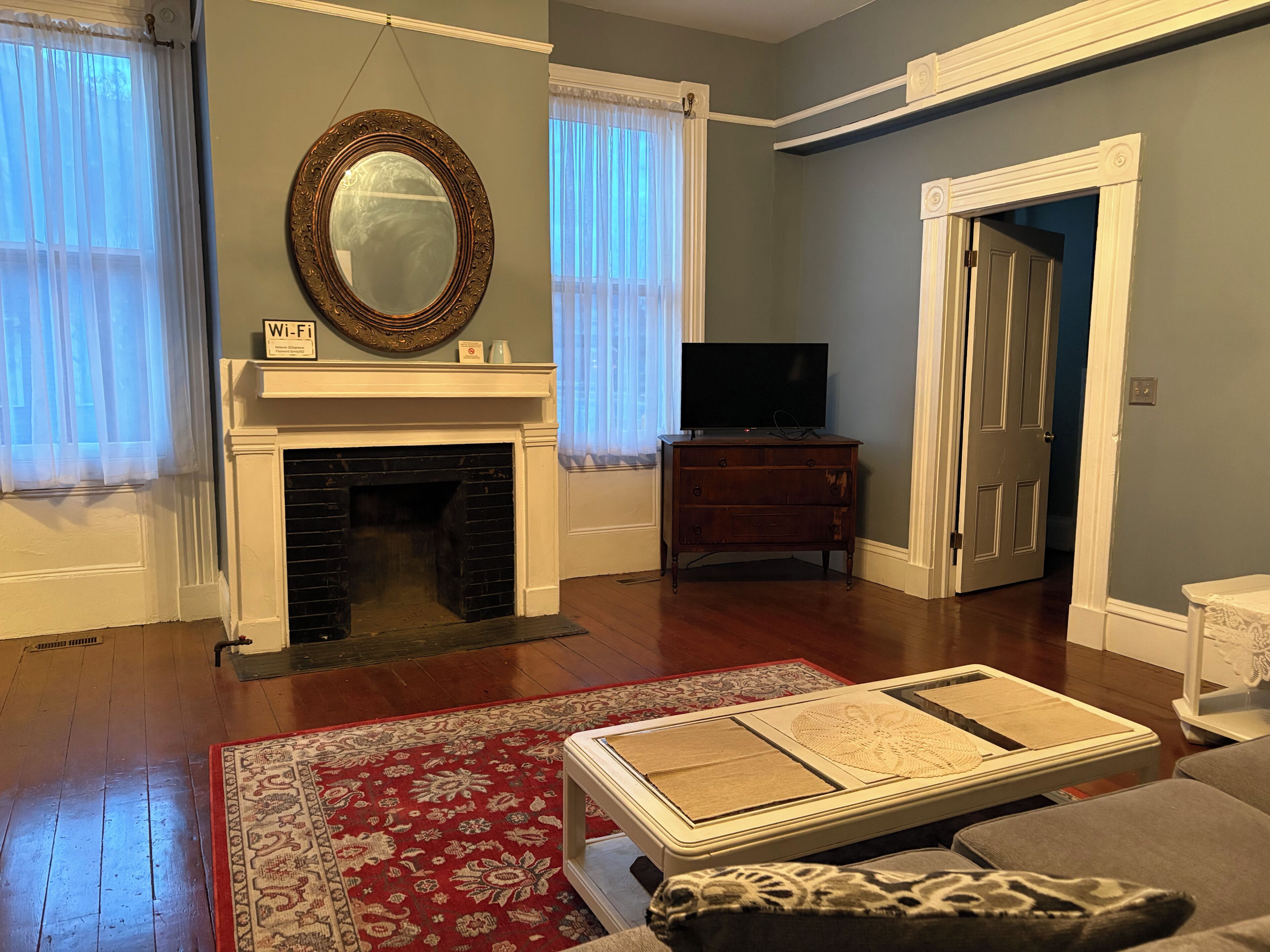 Un salon avec une cheminée, un téléviseur posé sur un meuble en bois et un tapis rouge à motifs.