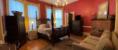 A bedroom with a four-poster bed, a chandelier, a fireplace, a sofa, and a dresser.
