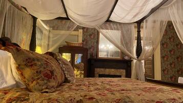 Una cama con ropa de cama floral, un cabecero de madera y cortinas blancas y translúcidas.