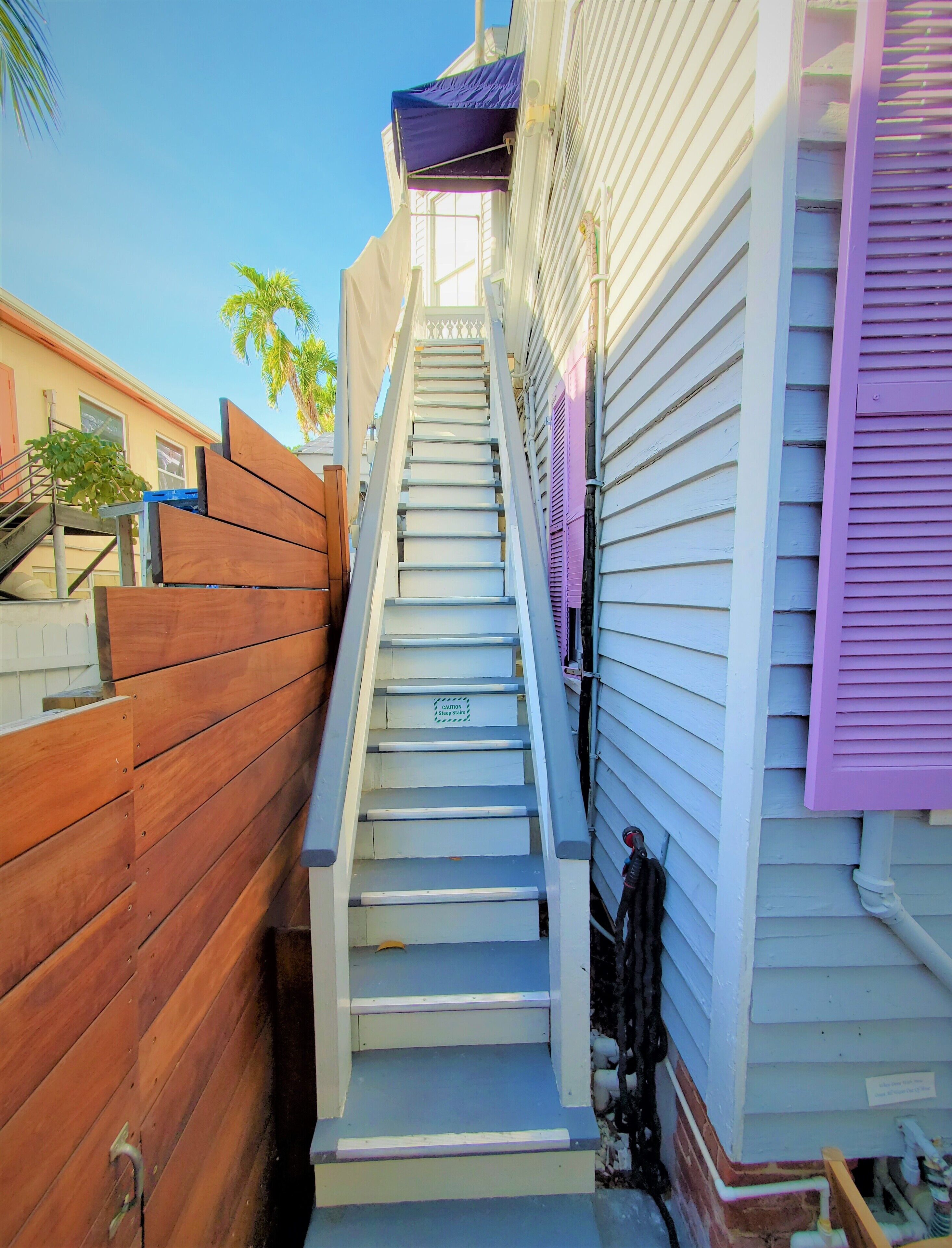 A staircase leading to a residential building with a wooden fence on one side and a white exterior with purple shutters.
