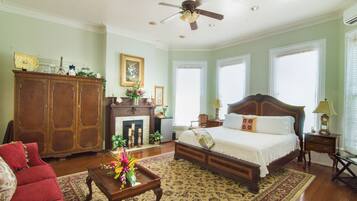 A bedroom with a large bed, a wooden dresser, a red armchair, a wooden coffee table, and a ceiling fan.