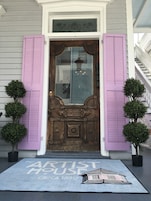 Una puerta principal con contraventanas moradas, un pequeño porche y un felpudo con la inscripción 'The Artist House Circa 1890'.