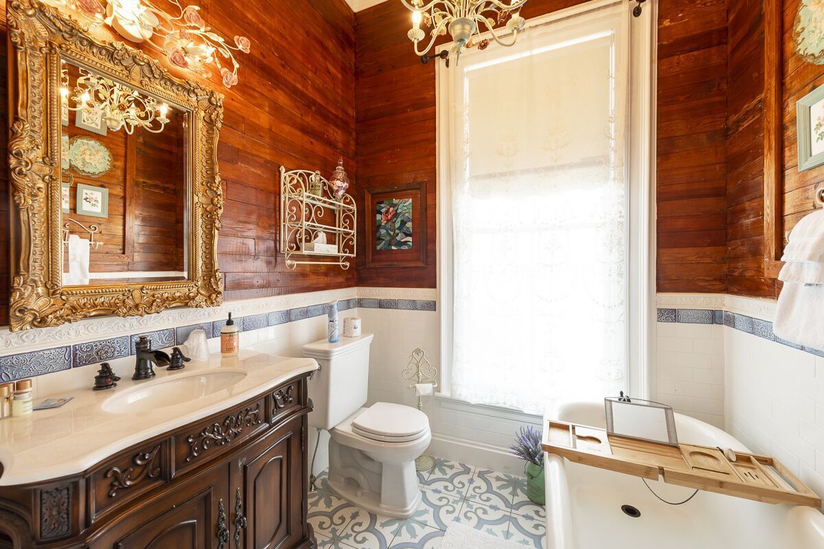 A bathroom with a wooden interior, a large ornate mirror, a white toilet, and a bathtub with a wooden tray.