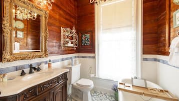 A bathroom with a wooden interior, a large ornate mirror, a white toilet, and a bathtub with a wooden tray.