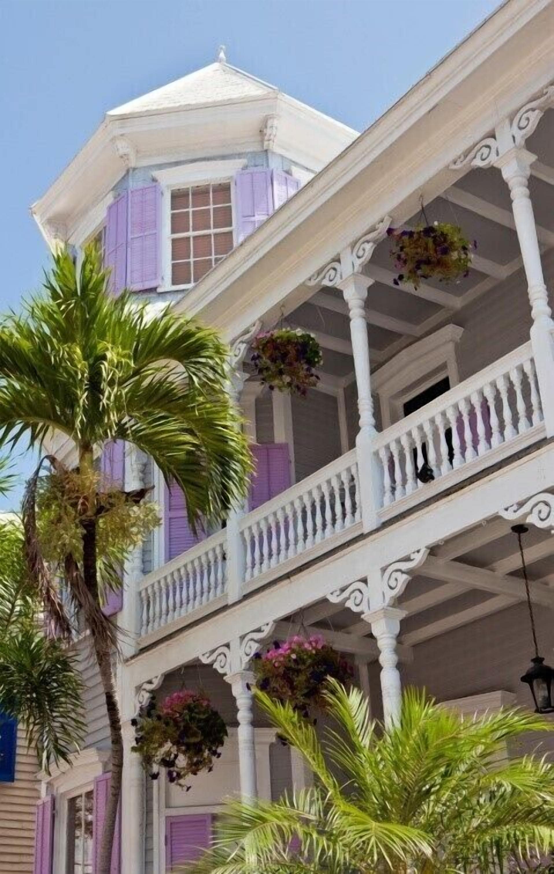 A two-story building with a balcony, white columns, and hanging flower baskets.