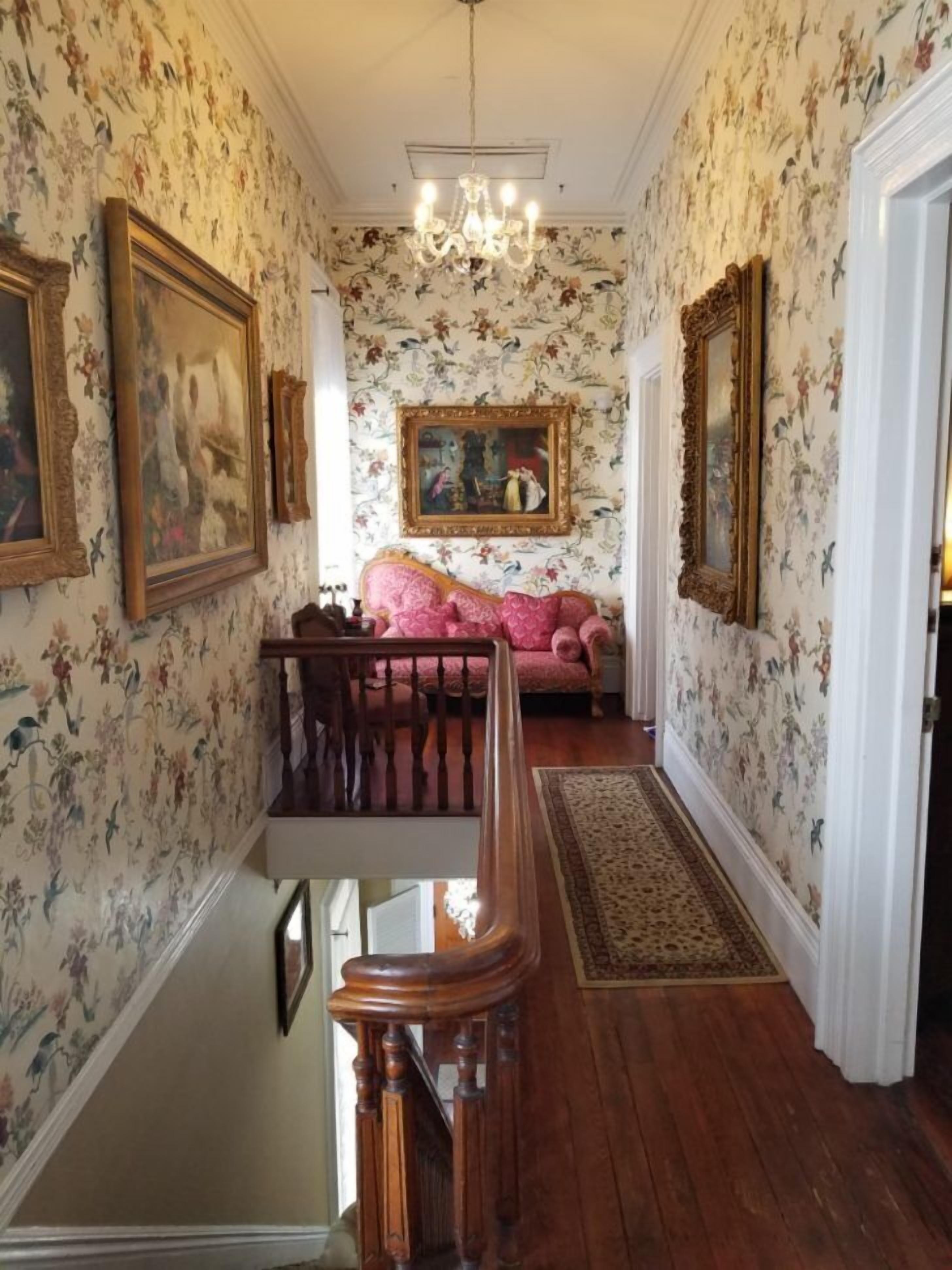 A hallway with floral wallpaper, a chandelier, a staircase, and a sofa.
