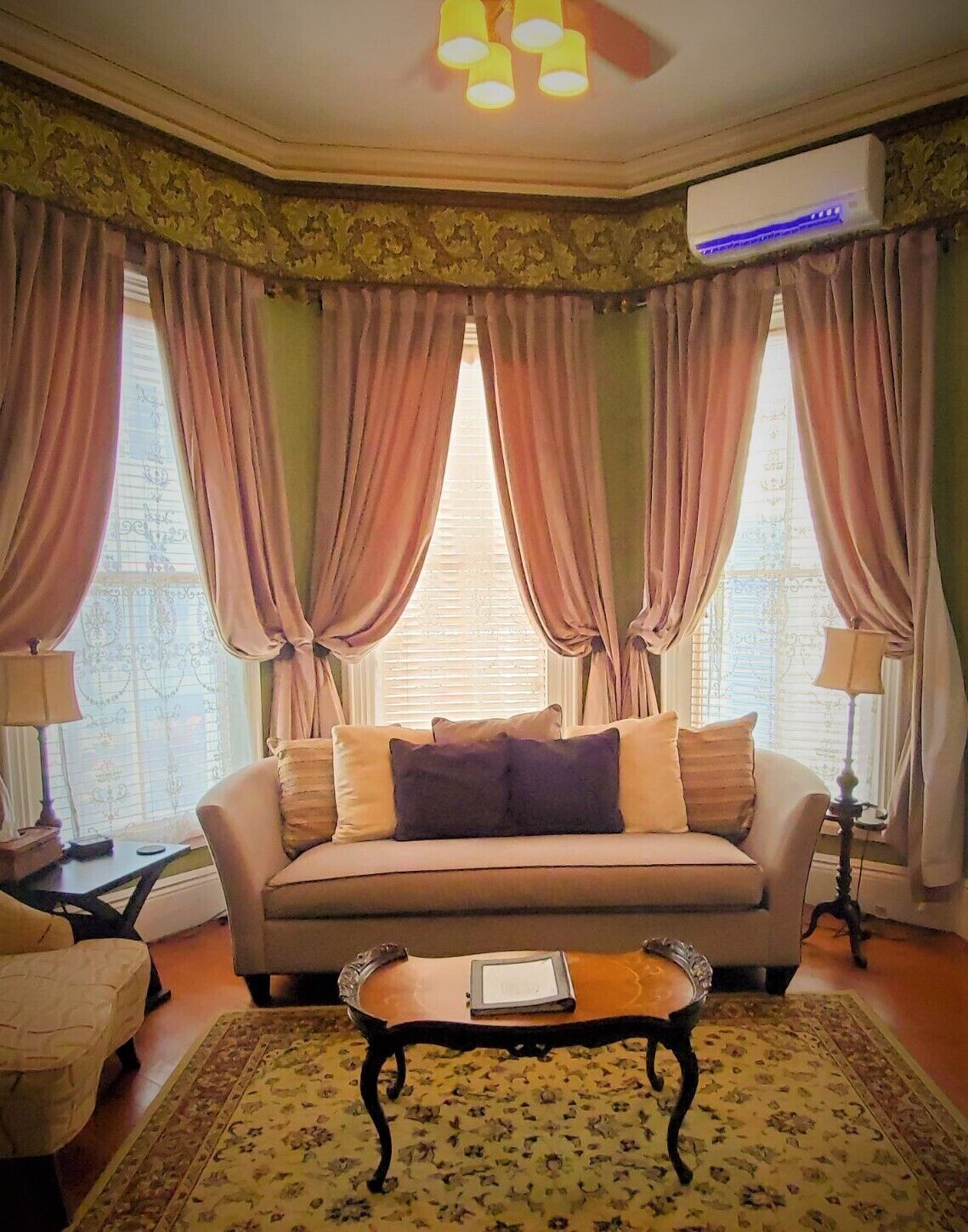 A living room with a sofa, a coffee table, and a patterned rug. There are two lamps and a ceiling fan.