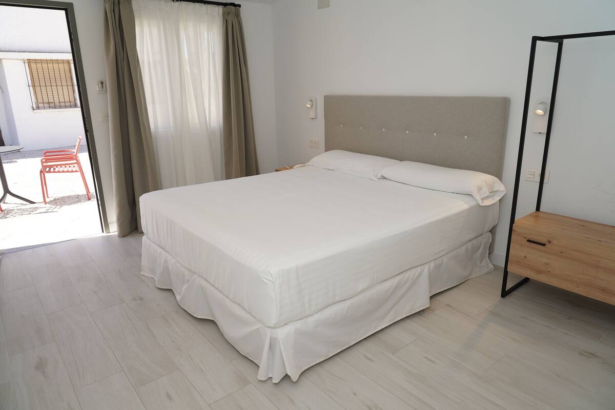 Una cama bien hecha con una mesita de noche de madera y un espejo.