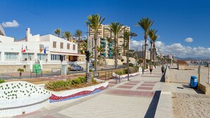 Un paseo marítimo frente a la playa con un camino adoquinado, palmeras y vistas a la playa y al océano.