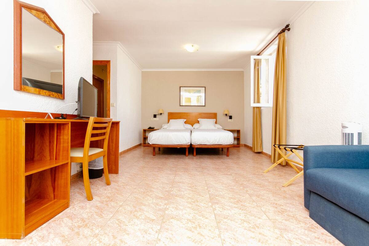 Una habitación de hotel con una cama, un escritorio con una silla, un televisor y un sofá azul.