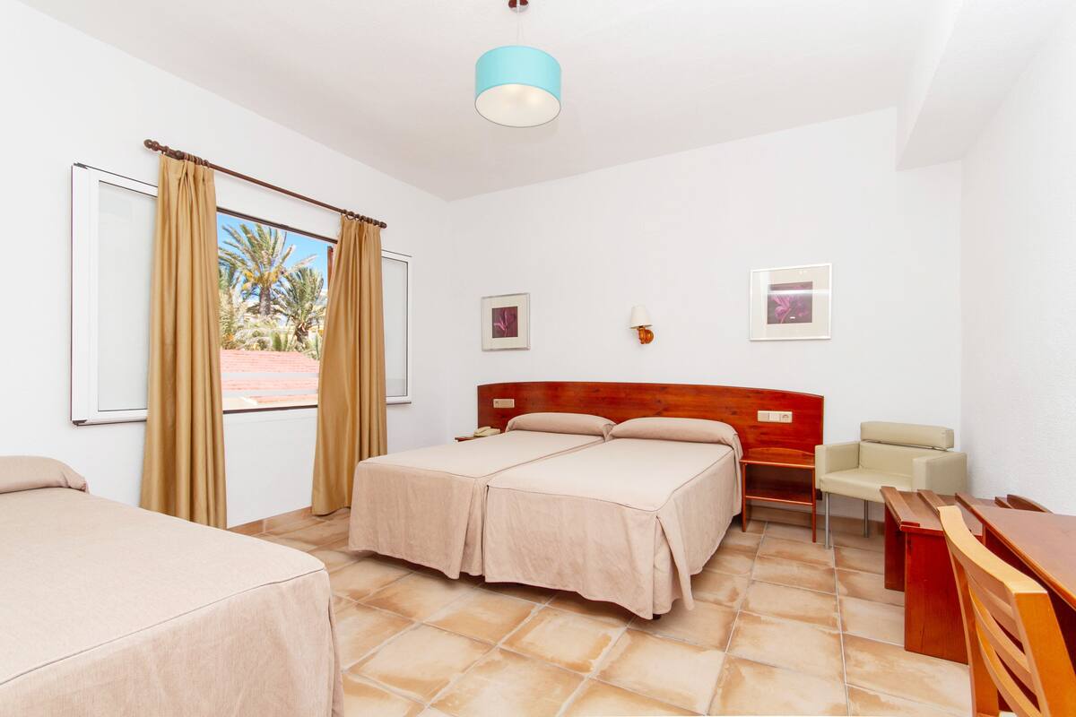 Habitación de hotel con dos camas, cabecero de madera, escritorio, una silla y ventana con cortinas.