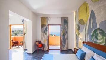 A hotel room with a bed, a chair, a table, and a view of the sea through a balcony.