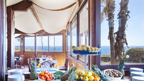 Een eetruimte met een gedekte tafel voor een maaltijd, met verschillende soorten fruit en gerechten, met uitzicht op de oceaan.