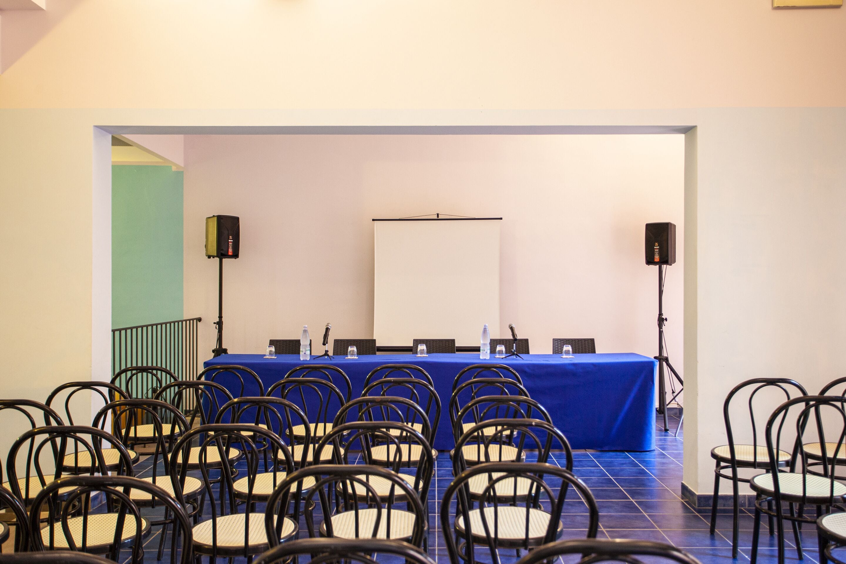 Een vergaderruimte met een blauwe tafel, stoelen, een whiteboard en speakers.