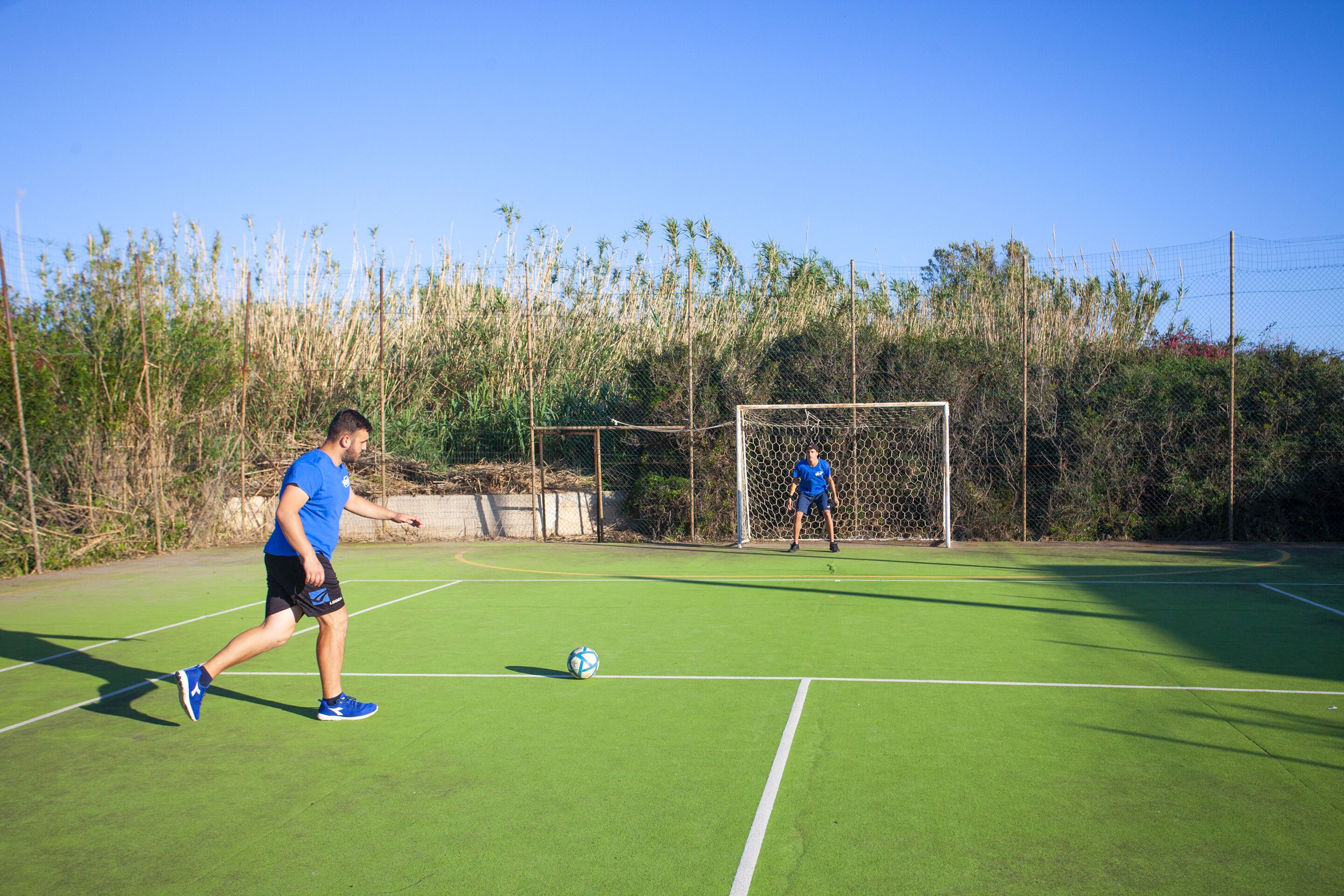 Un hombre juega al fútbol en un campo verde con un arco de portería al fondo.