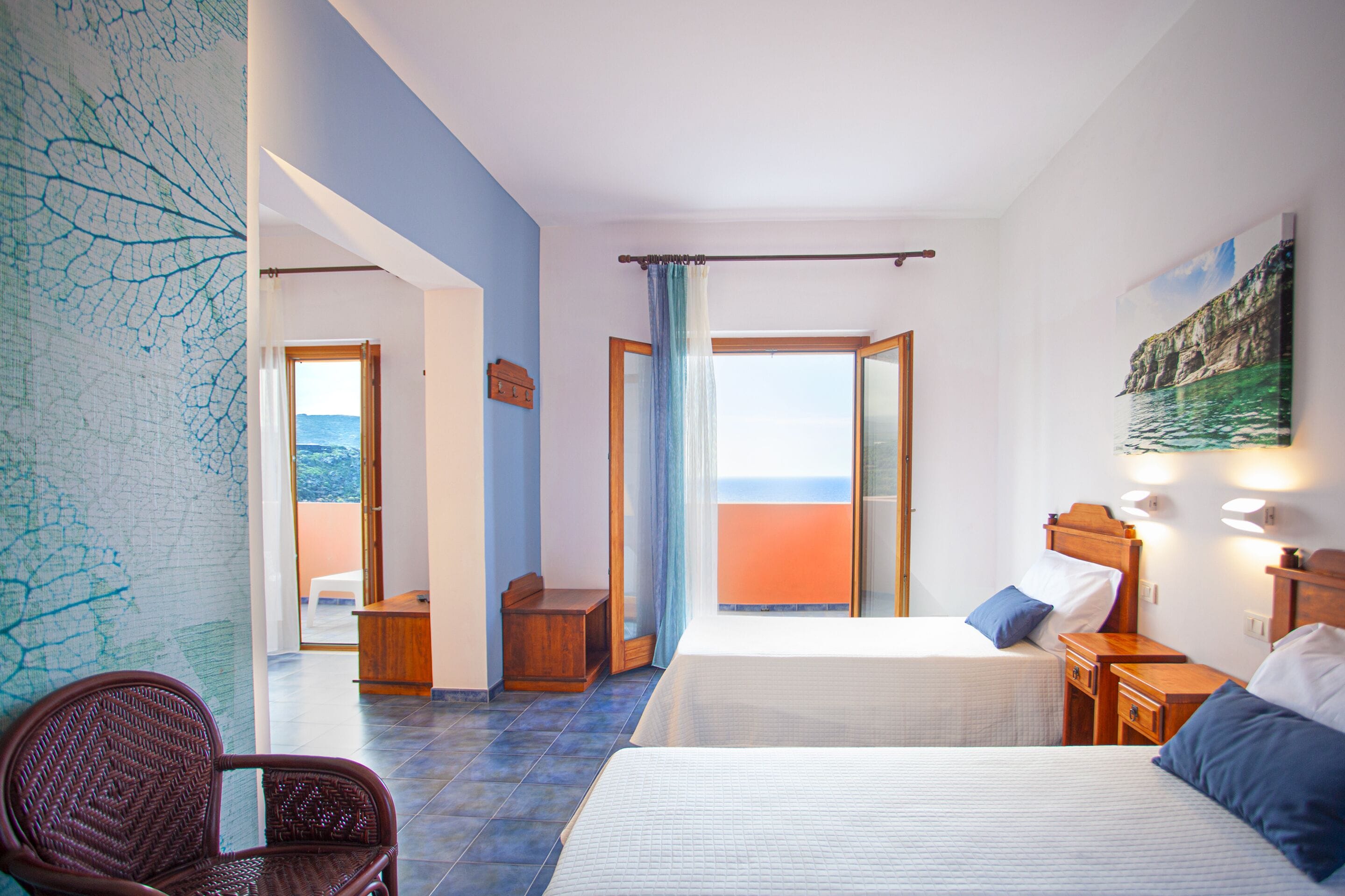 A hotel room with a bed, a chair, a desk, and a view of the sea.
