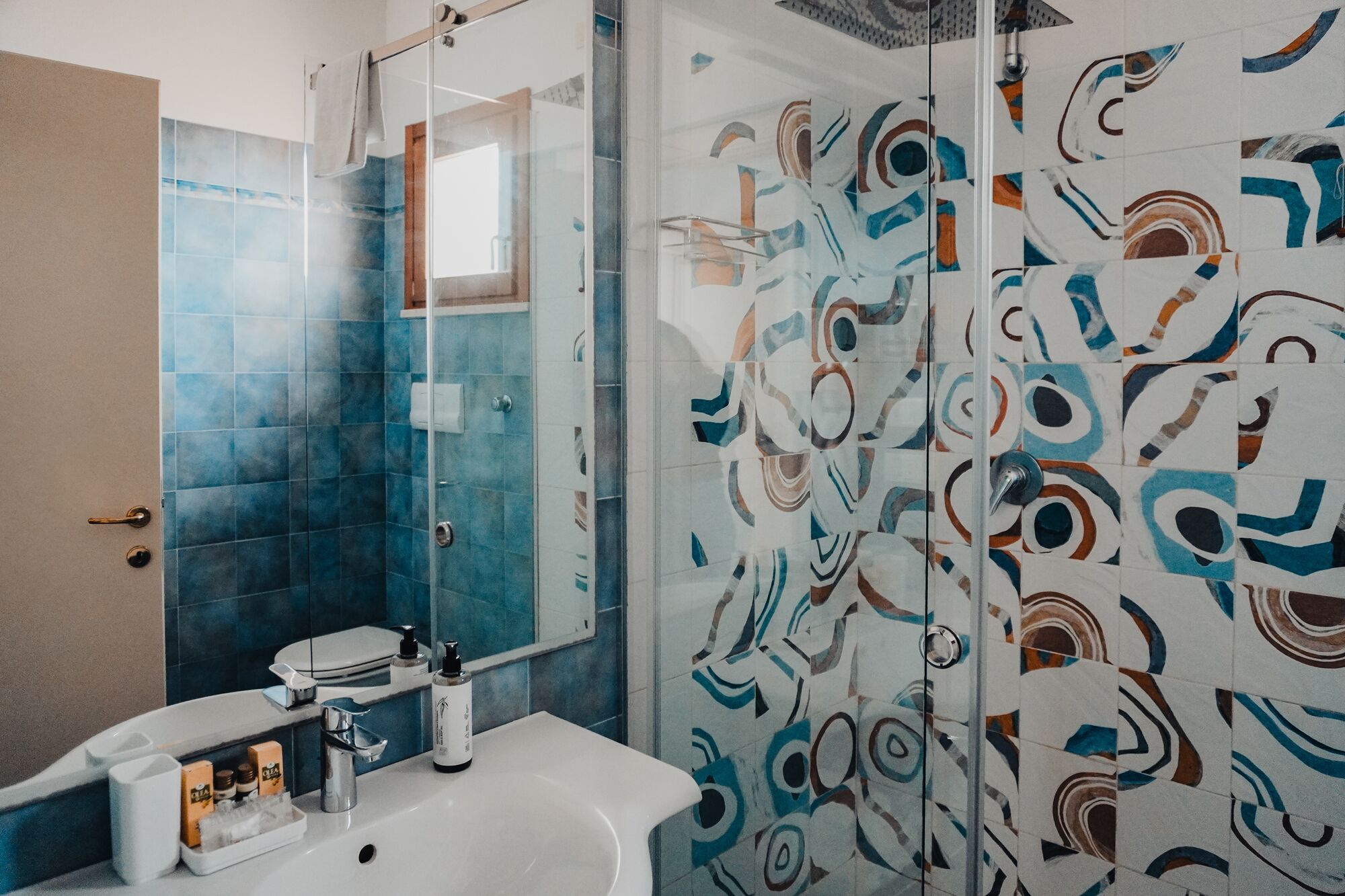 A bathroom with a glass shower enclosure, a white sink, and a toilet.