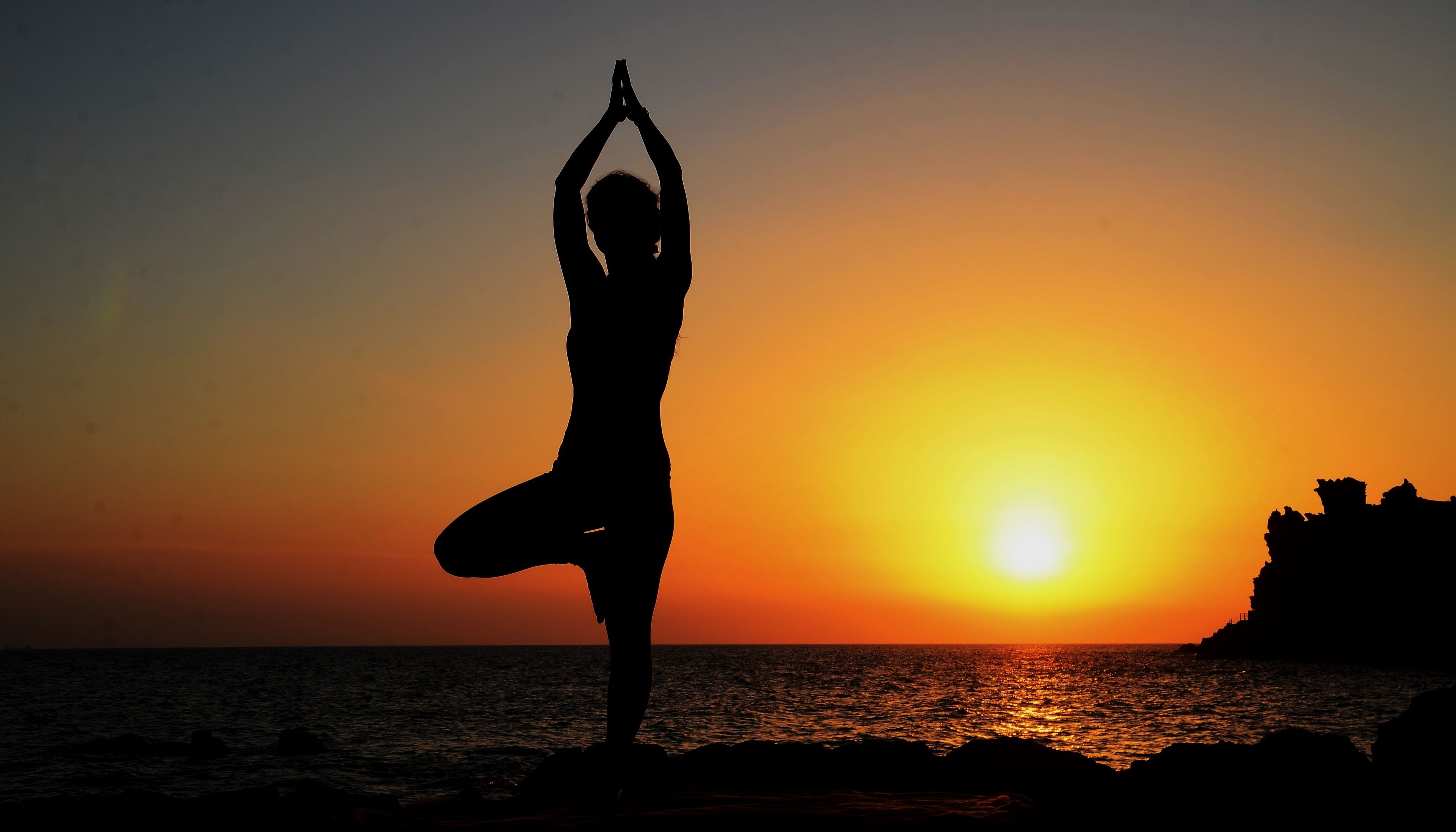 A silhouette of a person performing a yoga pose against a sunset backdrop.