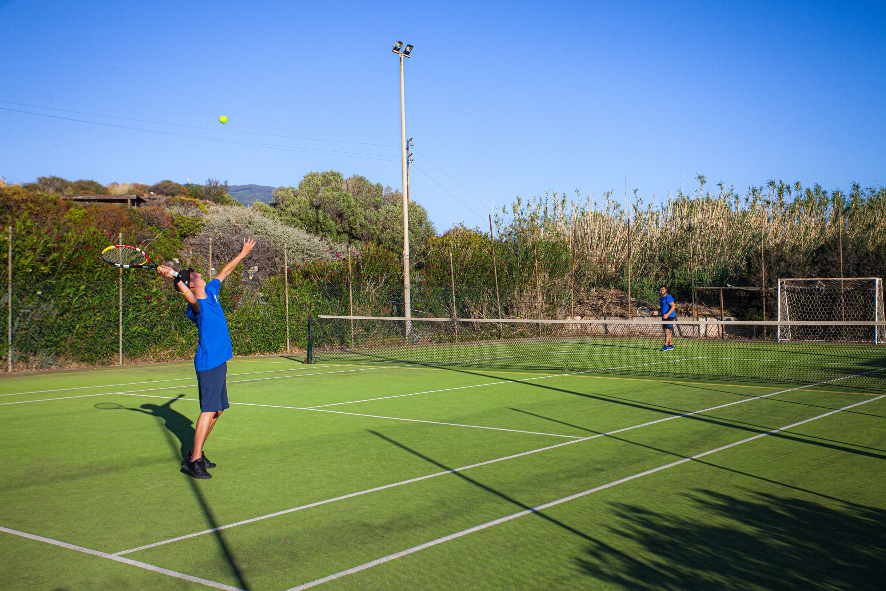 Een tennisbaan met twee spelers, een net en omliggend groen.