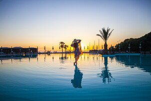 A person in a patterned dress standing in a calm pool with a sunset in the background.