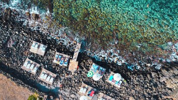 An aerial view of a beachside resort with multiple wooden deck areas, clear turquoise waters, and rocky shorelines.