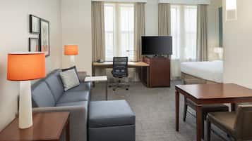 Habitación de hotel con sofá, reposapiés, escritorio, silla, televisor y cama.