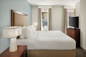 A hotel room with a large bed, a bedside table with a lamp, a TV, and a view of the outside. - Residence Inn by Marriott Savannah Downtown/Historic District (Savannah)