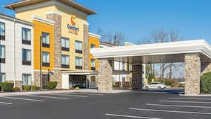 Un hotel Comfort Suites con diseño moderno, que presenta fachada de piedra, varios balcones y una zona de estacionamiento cubierta.