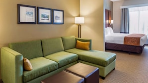 Habitación de hotel con un sofá verde, una mesita, una cama con una manta marrón y cuadros en la pared.