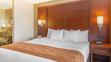 Een hotelkamer met een groot bed, een houten hoofdeinde, bedlampjes, een nachtkastje en een stoel in de hoek.