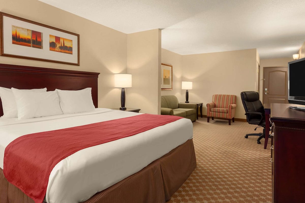 A hotel room with a large bed, two chairs, a desk, and a TV.