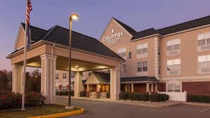 A Country Inn & Suites building with a covered entrance, multiple windows, and a flag. - Country Inn & Suites by Radisson, Doswell (Kings Dominion), VA (Doswell)