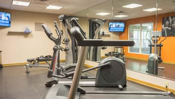 Un gimnasio con equipo de ejercicio, un muro espejado y un televisor en la pared.