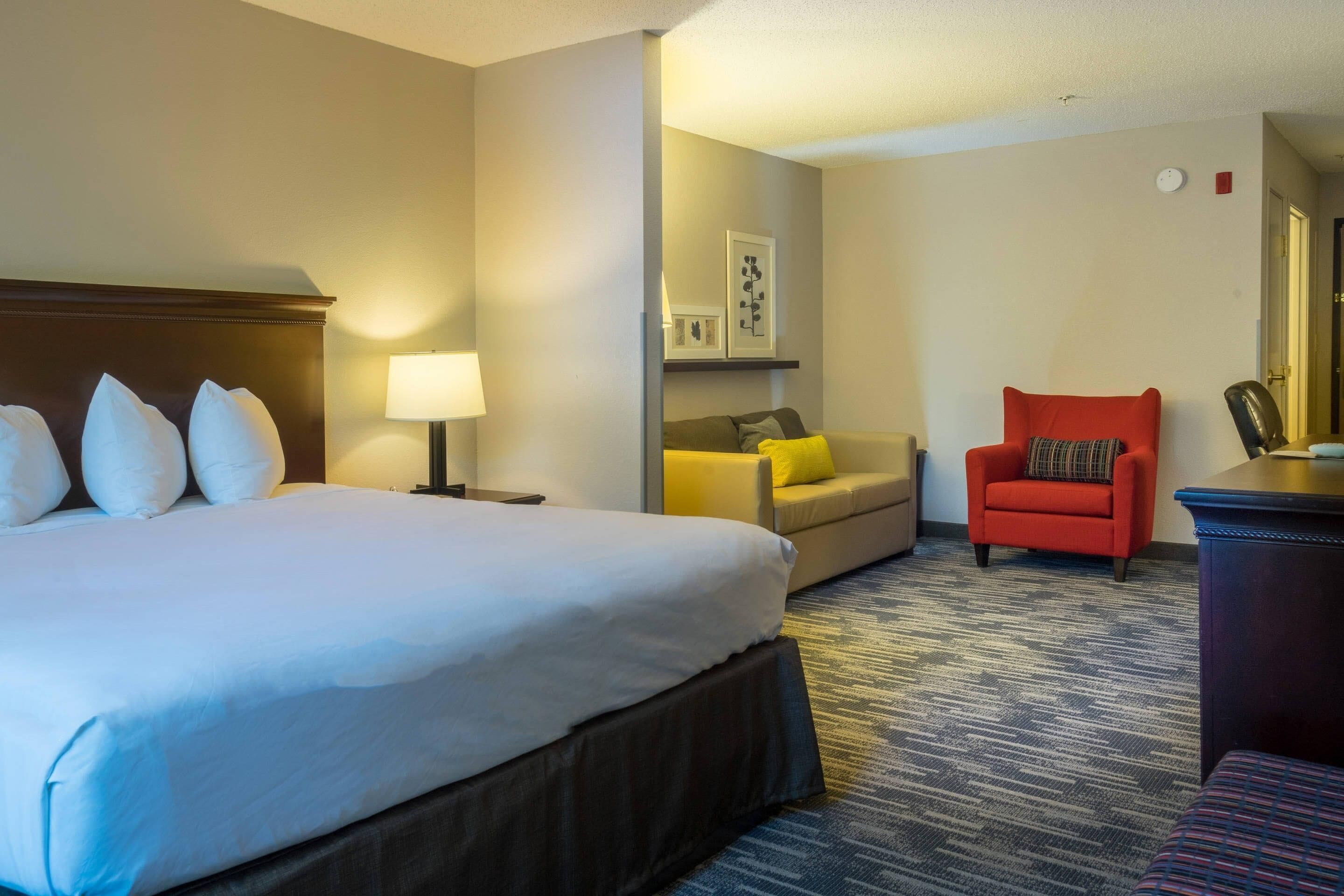 Een hotelkamer met een groot bed, een bank, een rode fauteuil en een bureau met een lamp.