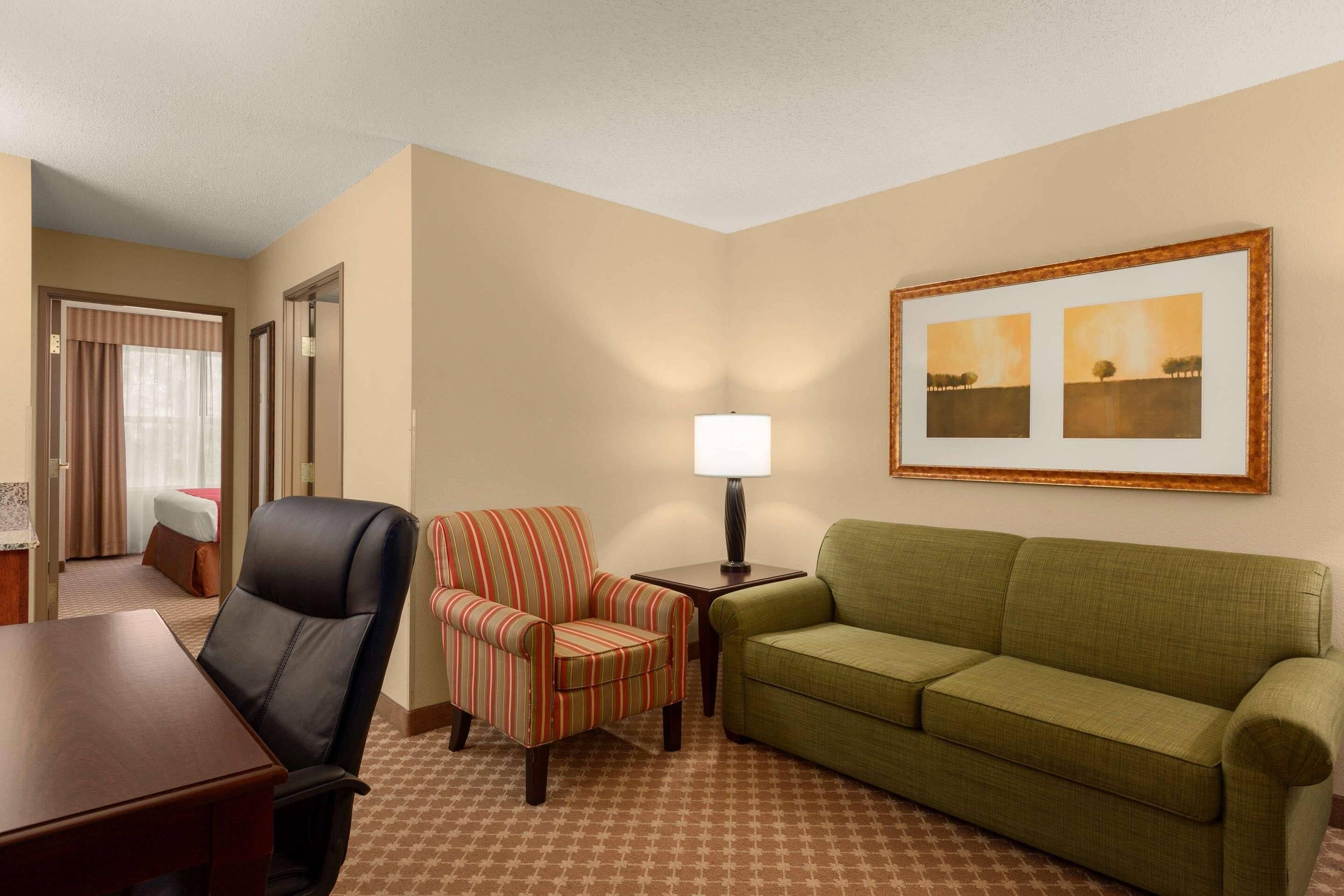 Una habitación de hotel con un sofá verde, un sillón a rayas y una mesa de madera.
