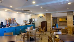 A restaurant with blue cabinets, wooden tables, and chairs. There are vending machines and a coffee machine on the counter. - Country Inn & Suites by Radisson, Doswell (Kings Dominion), VA (Doswell)