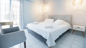 A modern bedroom with a large bed, a bedside table, a chair, and a window with curtains. - Aggelos Hotel (Messini)