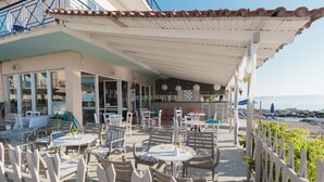 An outdoor seating area with tables and chairs, a covered section with a view of the sea, and a building with large windows and a balcony. - Aggelos Hotel (Messini)