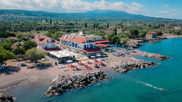 A coastal hotel with multiple buildings, a beach with umbrellas and sun loungers, and a rocky shoreline. - Aggelos Hotel (Messini)