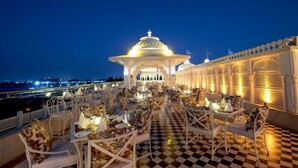 A rooftop dining area with checkered flooring and white furniture, overlooking a cityscape at dusk. - Radisson Blu Udaipur Palace Resort & Spa (Udaipur)