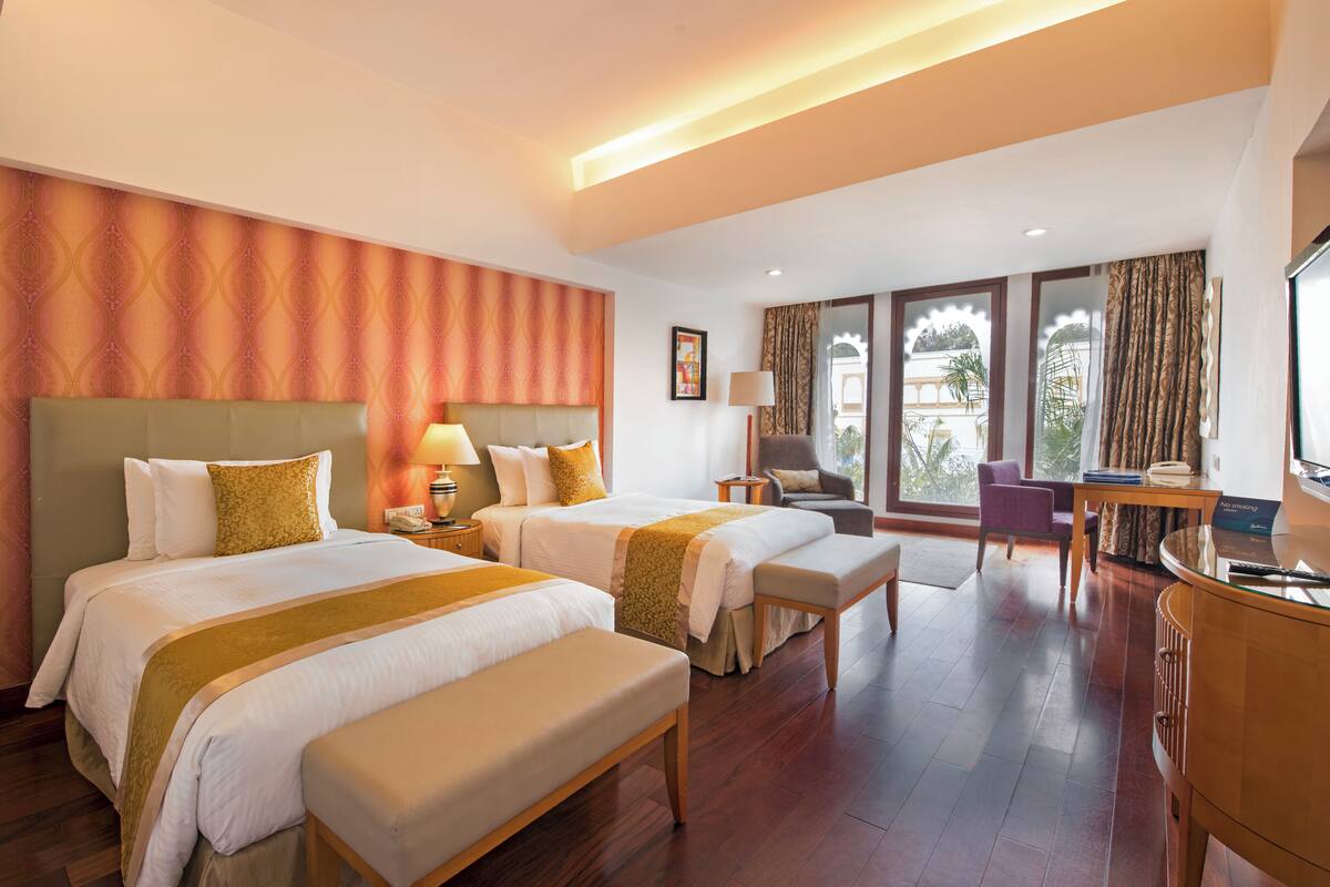 Ein Hotelzimmer mit zwei Betten, einem Schreibtisch, einem Stuhl und Blick ins Freie.