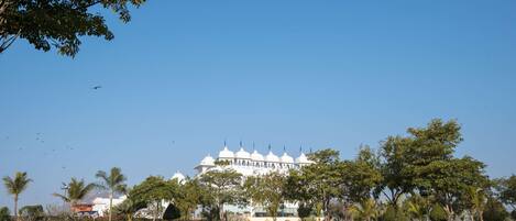 A large, white building with multiple domes and spires, surrounded by a well-maintained lawn and palm trees.