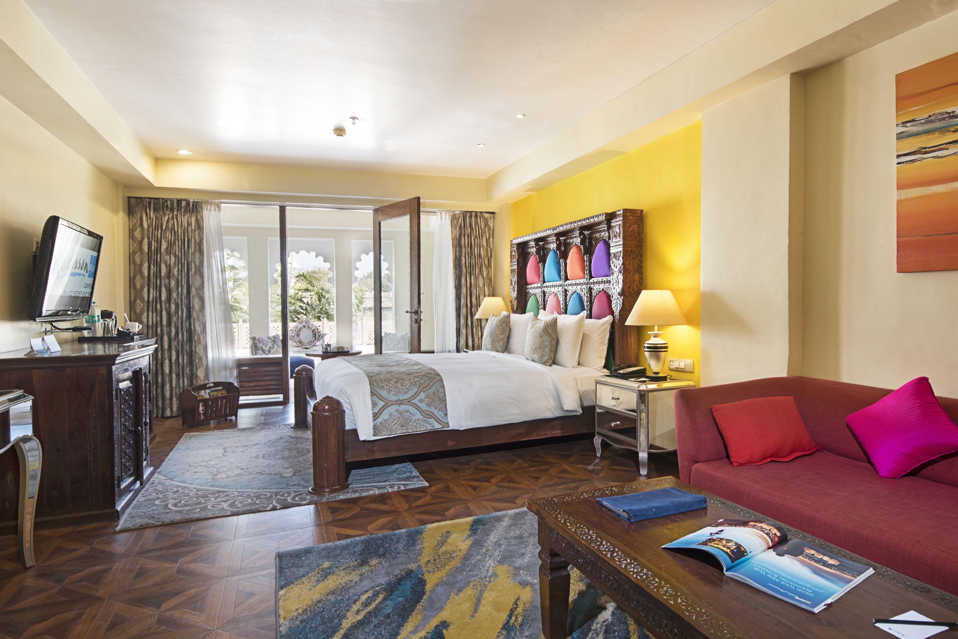 A hotel room with a bed, a sofa, a coffee table, a desk, and a TV.