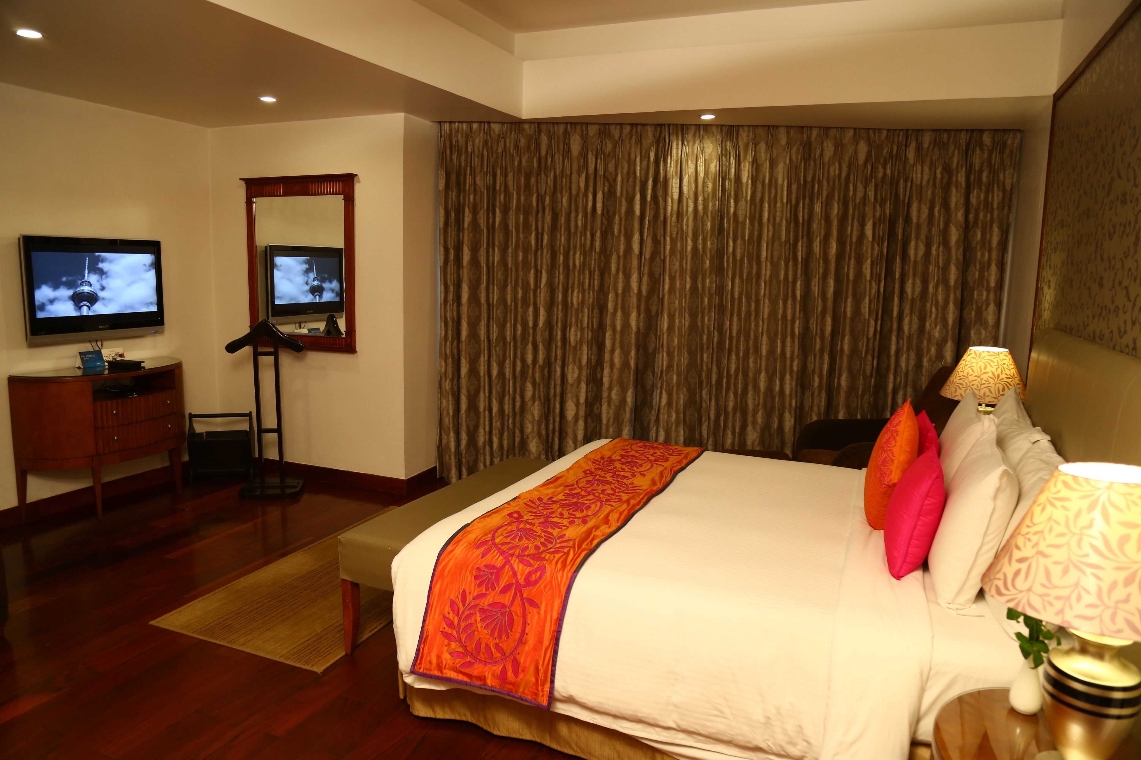 A hotel room with a large bed, a television, a desk, and a mirror.