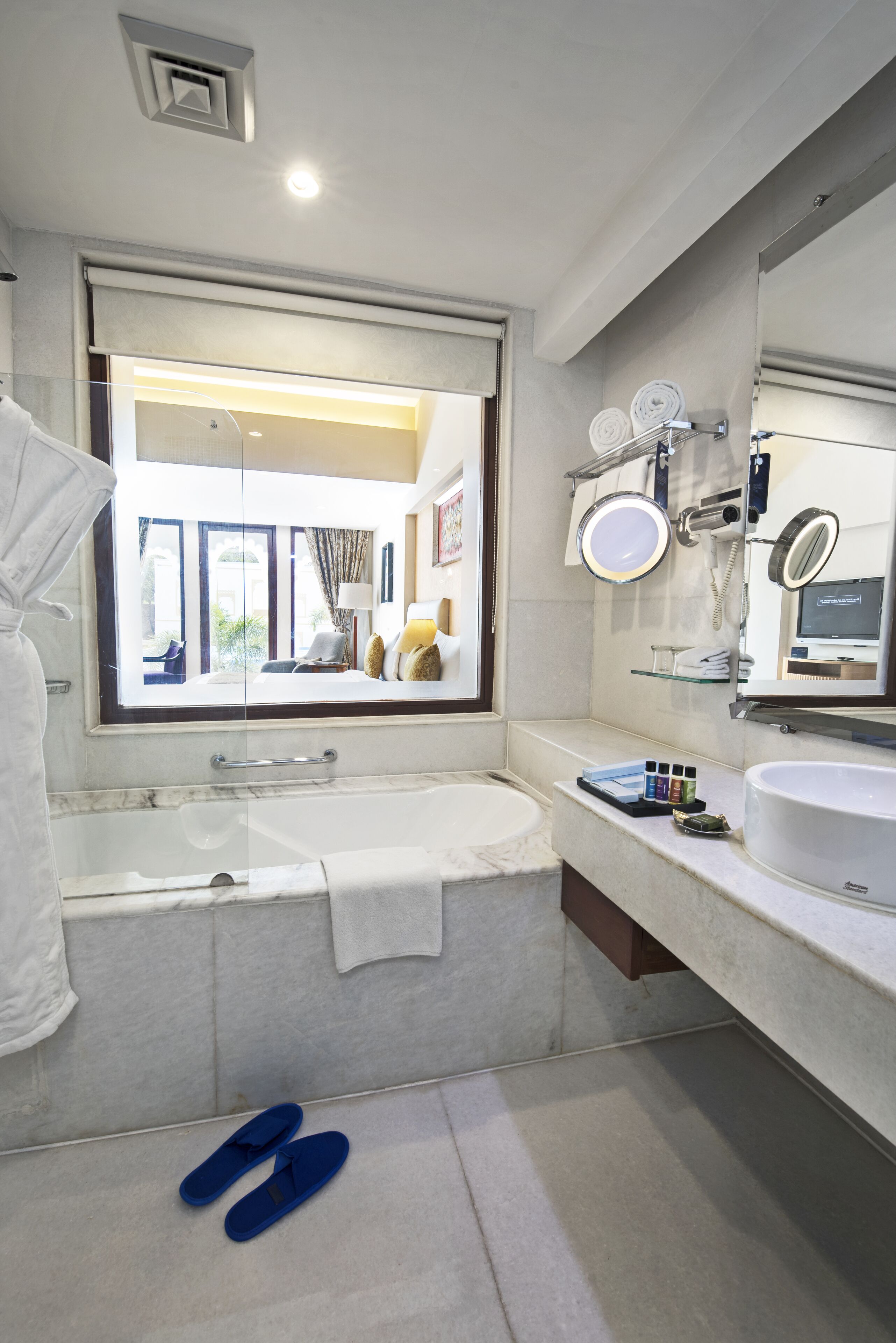 A modern bathroom with a large bathtub, a vanity with a mirror, and a window offering a view of the room.