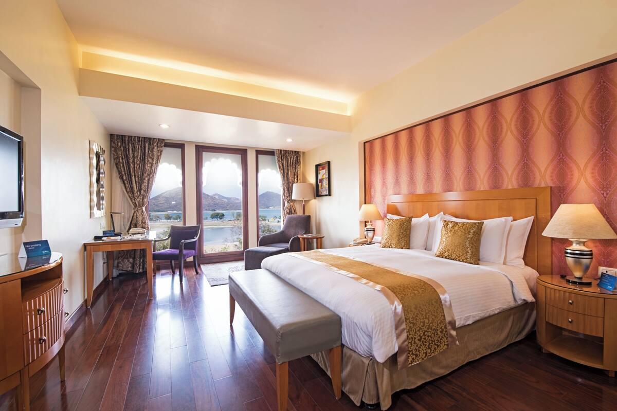 Ein Hotelzimmer mit einem großen Bett, einem Schreibtisch mit Computer, einem Sessel und Blick auf die Berge.