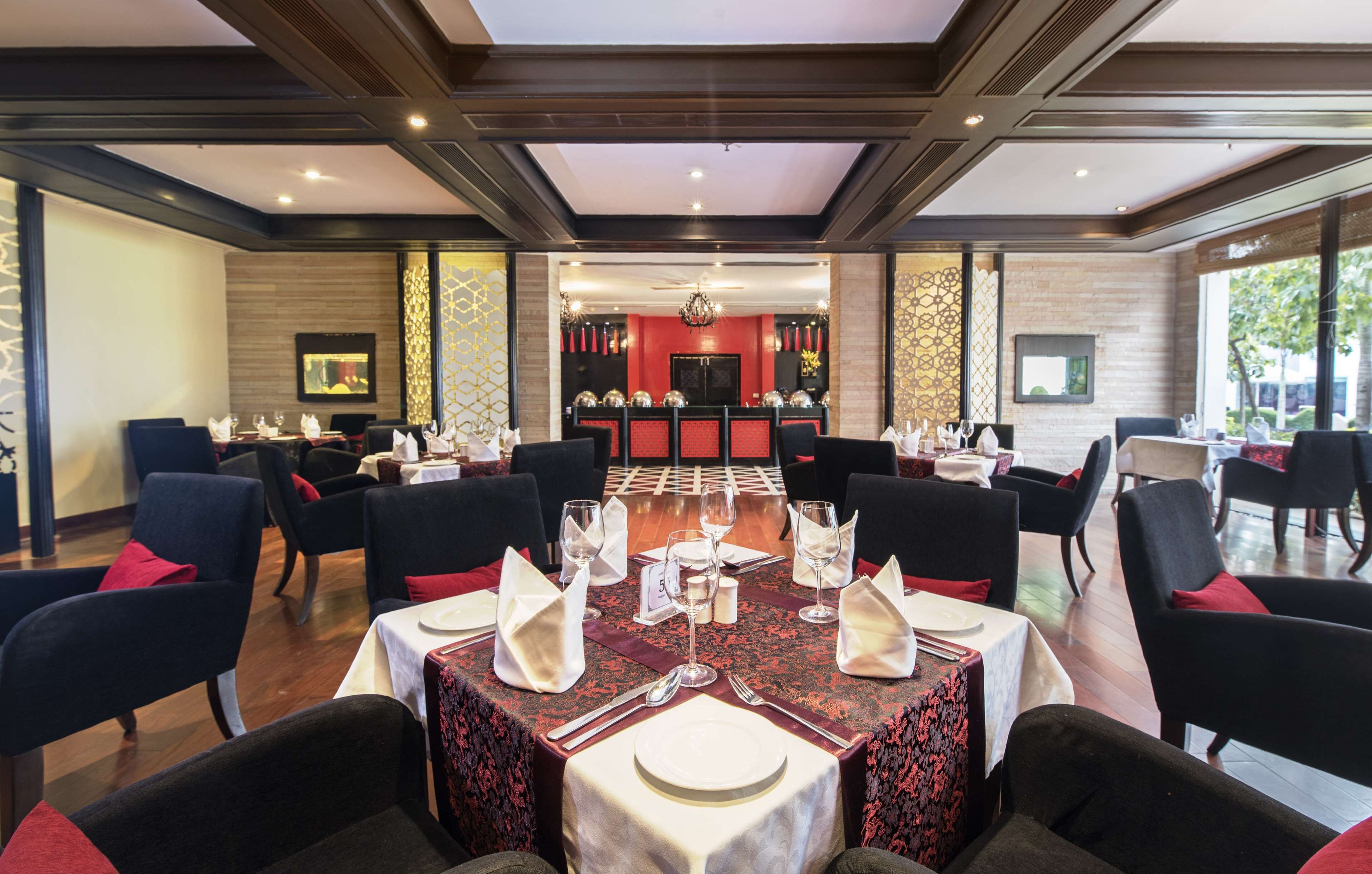 A dining area with tables set for four, each with white tablecloths, red napkins, and silverware.