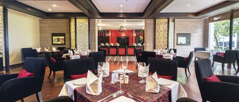 Un espace repas avec des tables dressées pour quatre personnes, chacune agrémentée d’une nappe blanche, de serviettes rouges et de couverts en argent.